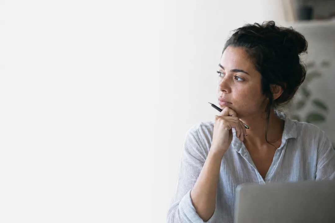 Thoughtful woman at her workplace, looking away from the screen in a moment of reflection